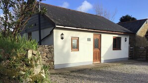 A small, single-story building with a stone wall and a gravel driveway. - Tregonning Lodge (Helston)
