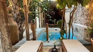 Zona de piscina amb dues cadira de vella, una banca de pedra amb un vas i una paret de pedra.