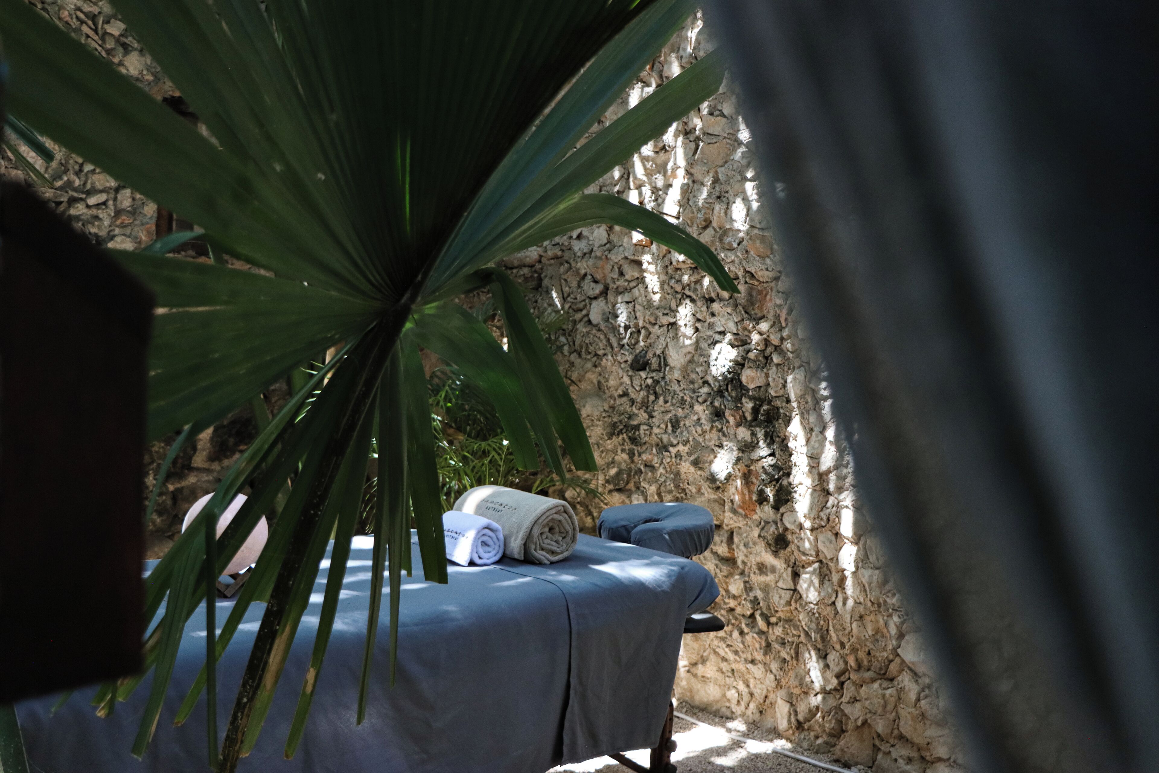 A massage table with a towel, a stone wall, and a palm tree in the background.