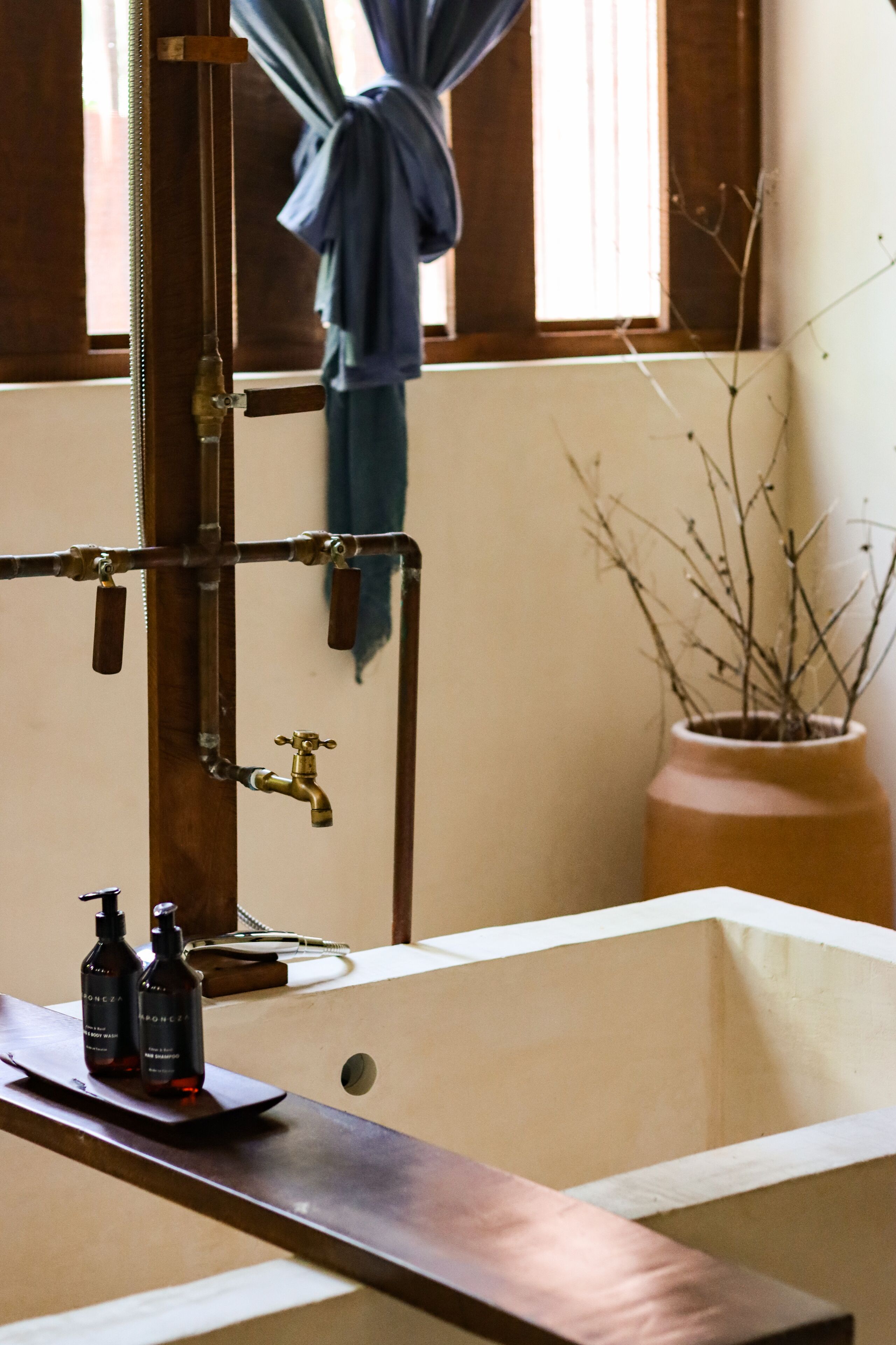 Un baño con una bañera de madera, un perchero y una planta en maceta.