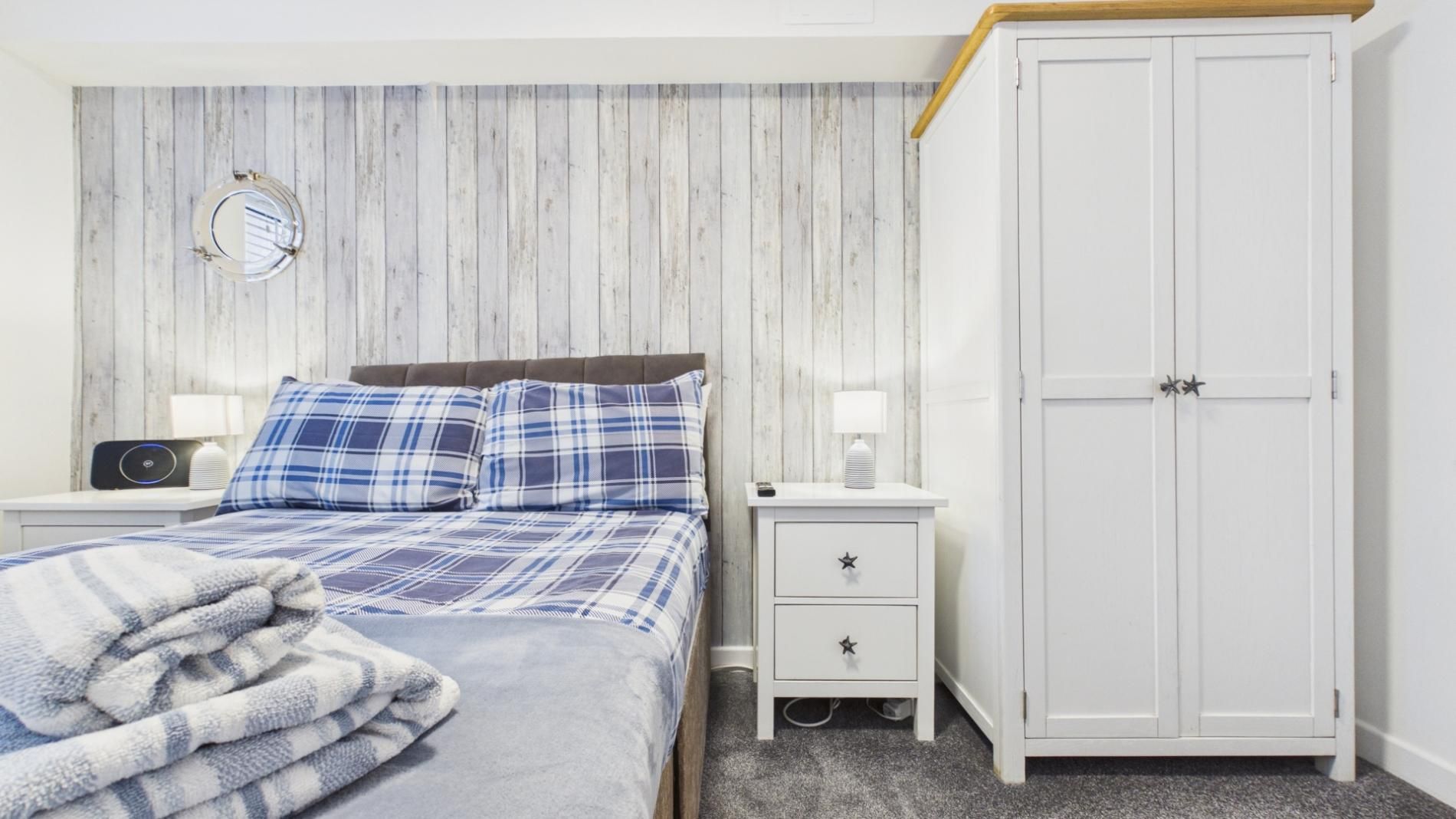 A bedroom with a bed, a nightstand, a wardrobe, and a mirror on the wall.