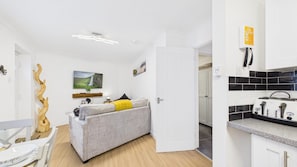 A compact living space with a sofa, a dining table, a kitchen area with a toaster, and a white door leading to another room.