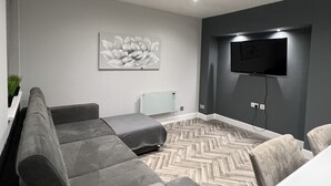 Un soggiorno moderno con un divano grigio, un pavimento a spina di pesce, una TV a parete e un'opera d'arte floreale.