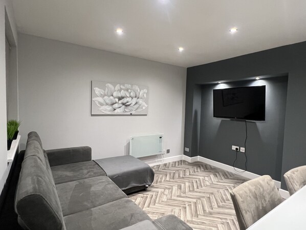 A modern living room with a grey sofa, a herringbone-patterned floor, a wall-mounted TV, and a floral artwork. - The Broadway Retreat With Parking (Herne Bay)