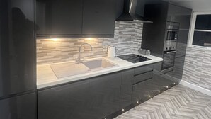 Una cucina moderna con mobili scuri, lavello in acciaio inossidabile, piano di lavoro nero, schienale piastrellato ed elettrodomestici integrati come microonde e forno.