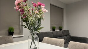 Un soggiorno moderno con un tavolo bianco, un vaso trasparente con fiori rosa e un divano grigio.