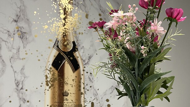 Una bottiglia di champagne con etichetta e un vaso di vetro con fiori rosa.