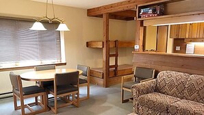 Una sala de estar acogedora con una mesa de comedor redonda de madera, dos sillas, un sofá estampado y una pequeña mesa de centro.