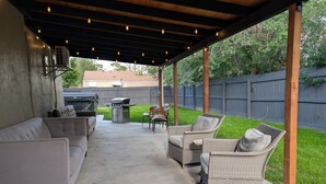 An outdoor patio with a covered seating area, a grill, and a concrete floor.