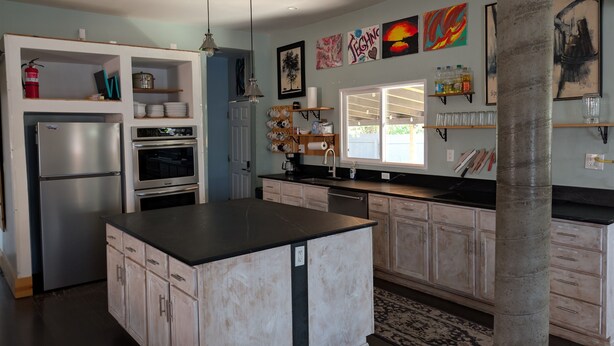 A modern kitchen with a central island, built-in oven, and a large window.