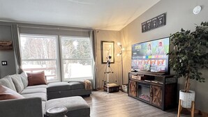 Ett vardagsrum med ett stort fönster, en soffa, en tv och en växt.