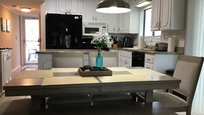Eine moderne Küche mit weißen Schränken, einem schwarzen Kühlschrank, einer Kaffeemaschine und einer Insel mit Blumen in einer Vase.