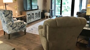 Ein Wohnzimmer mit einer Couch, Sesseln, einem Fernseher und einem kleinen Tisch mit einer Lampe.