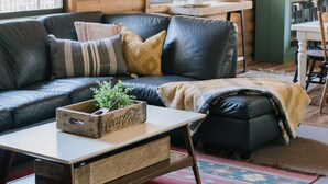 Interior acogedor de una cabaña de madera con un sofá de cuero, una mesa de centro de madera y un armario verde.