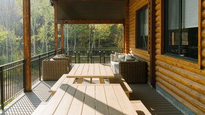 Una terraza de madera con una mesa de picnic y mobiliario de mimbre, con vistas a un área boscosa.