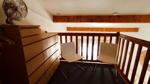 Une petite pièce avec une commode en bois, deux chaises et un ventilateur de plafond.