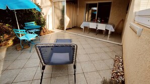 Une terrasse avec une table et des chaises, un parasol bleu et une porte-fenêtre coulissante donnant sur une pièce.