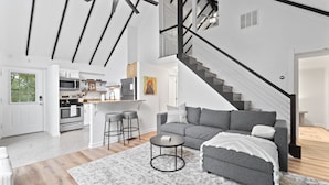 A modern living room with a grey sofa, a coffee table, and a staircase leading to an upper level. - Escape to Shenandoah River, Hot Tub after a Hike!  (Front Royal)