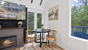A cozy living room with a fireplace, a round table with chairs, a large window with a view of a deck, and a painting on the wall. - Escape to Shenandoah River, Hot Tub after a Hike!  (Front Royal)