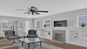 A living room with a fireplace, a ceiling fan, and a television on a mantel.