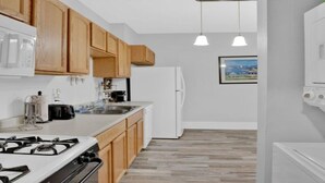 A modern kitchen with wooden cabinets, a white refrigerator, a stove, and pendant lighting.