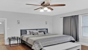 A bedroom with a bed, a ceiling fan, a bedside table, and a window with curtains.