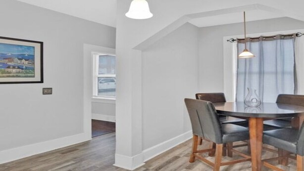 A dining area with a round table, chairs, pendant lights, and a window with curtains.