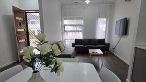 Ein modernes Wohnzimmer mit einem weißen Tisch, einer Couch und einem an der Wand befestigten Fernseher.