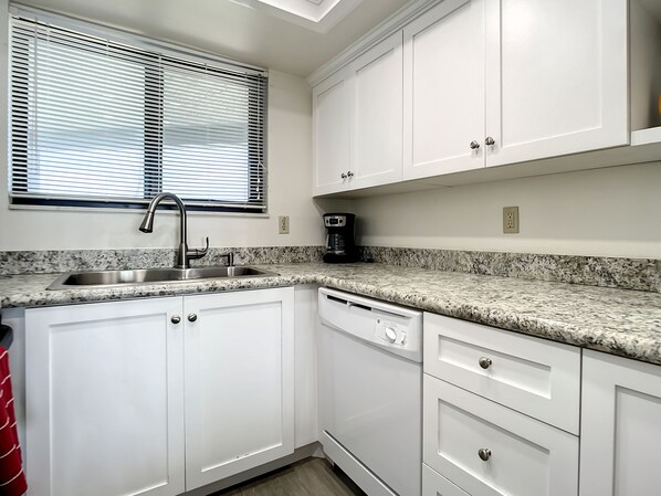 A kitchen with white cabinets, a granite countertop, a stainless steel sink, and a coffee maker.