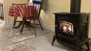 A cozy room with a table covered in a striped tablecloth, a chair, a black wood-burning stove, and a lamp. - Tiny Tuck-in - Downtown Belfast (Belfast)