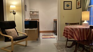 A living room with a TV on a stand, a dining table with a striped tablecloth, and a kitchen area with a sink and cabinets. - Tiny Tuck-in - Downtown Belfast (Belfast)