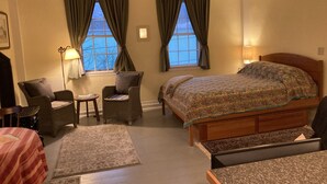 A cozy hotel room with a bed, two chairs, a small table, and two windows with curtains. - Tiny Tuck-in - Downtown Belfast (Belfast)