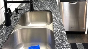 Ett kök med vita skåp, en diskho i rostfritt stål, en svart mikrovågsugn och en diskmaskin.