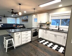 A modern kitchen with white cabinets, a black countertop, and a black and white striped rug. - Southfork home sleeps 12 private setting w/ hot tub (Ririe)