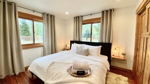 Un dormitorio con una cama grande, suelo de madera y vistas a un bosque a través de las ventanas.