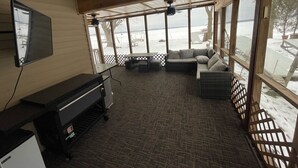 Ein Zimmer mit großem Fenster mit Blick auf eine verschneite Landschaft, ein Sofa, ein kleiner Tisch und ein Klavier.