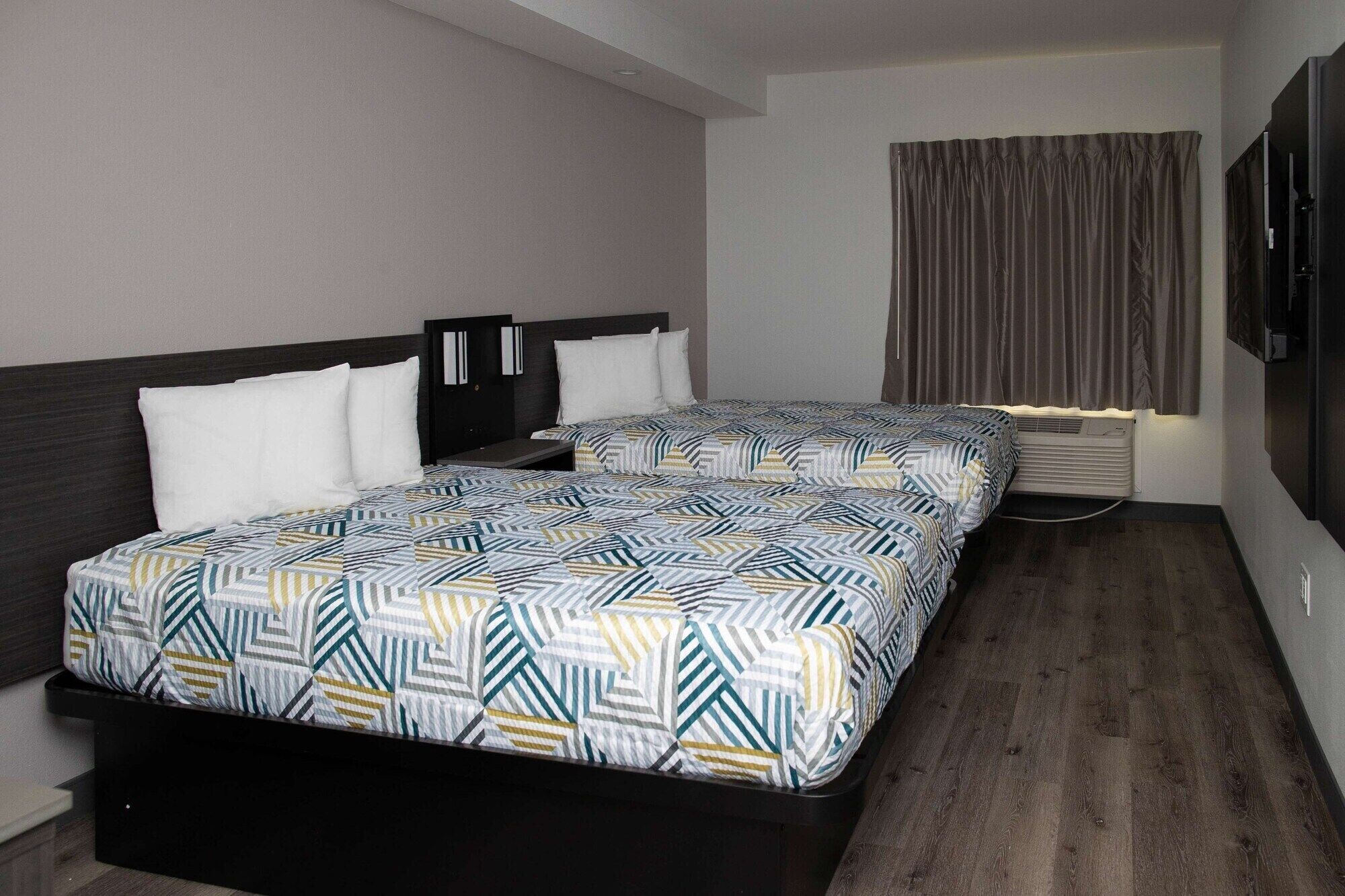 Une chambre d’hôtel avec deux lits, une tête de lit sombre, une grande fenêtre avec des rideaux et un système de climatisation intégré.