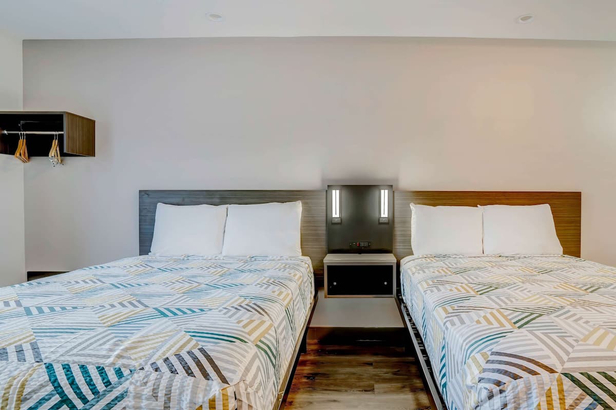 Een hotelkamer met twee bedden, een nachtkastje met een lamp en een kledingkast.