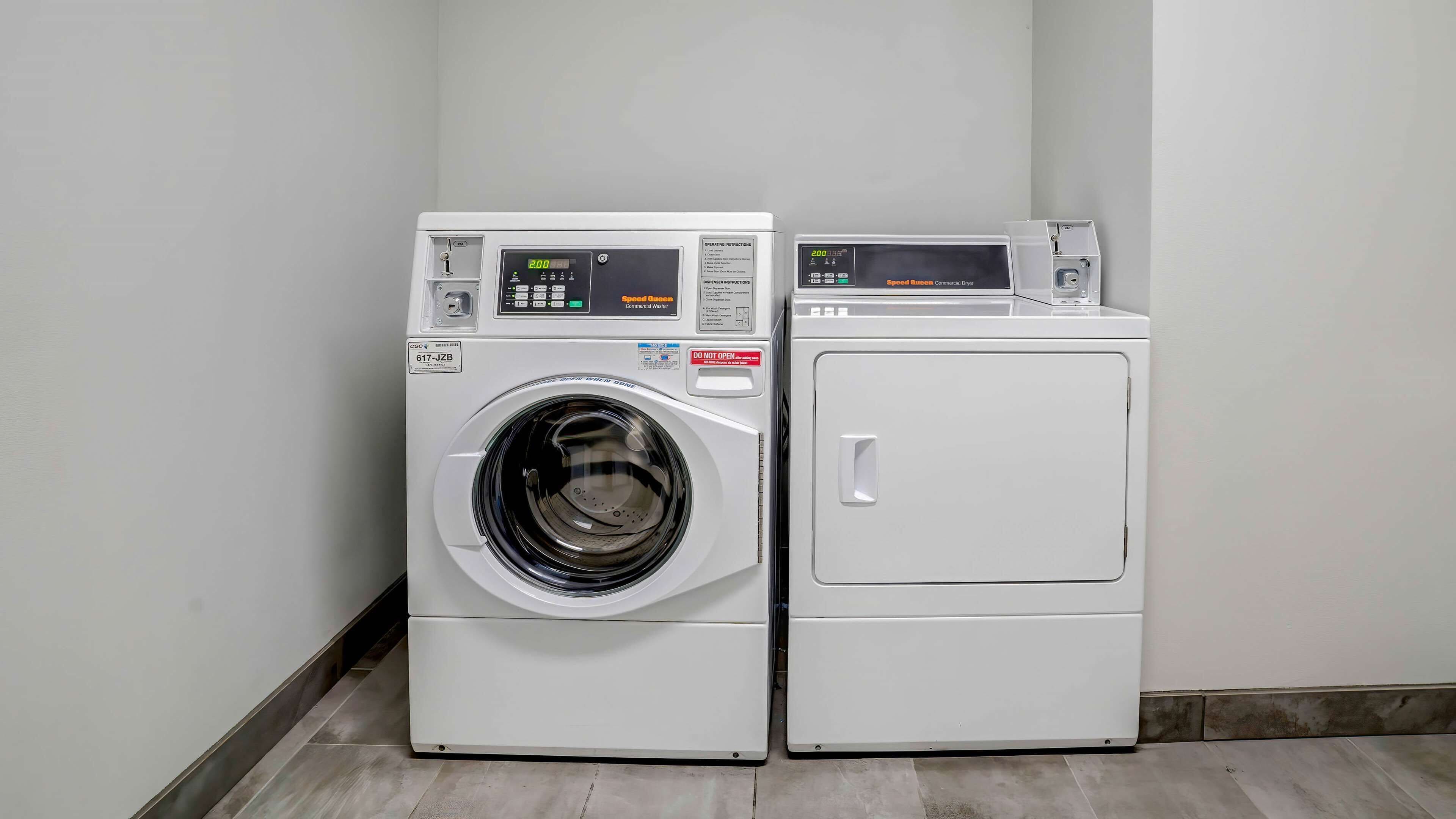 A commercial washer and dryer unit in a clean, white-walled laundry room.