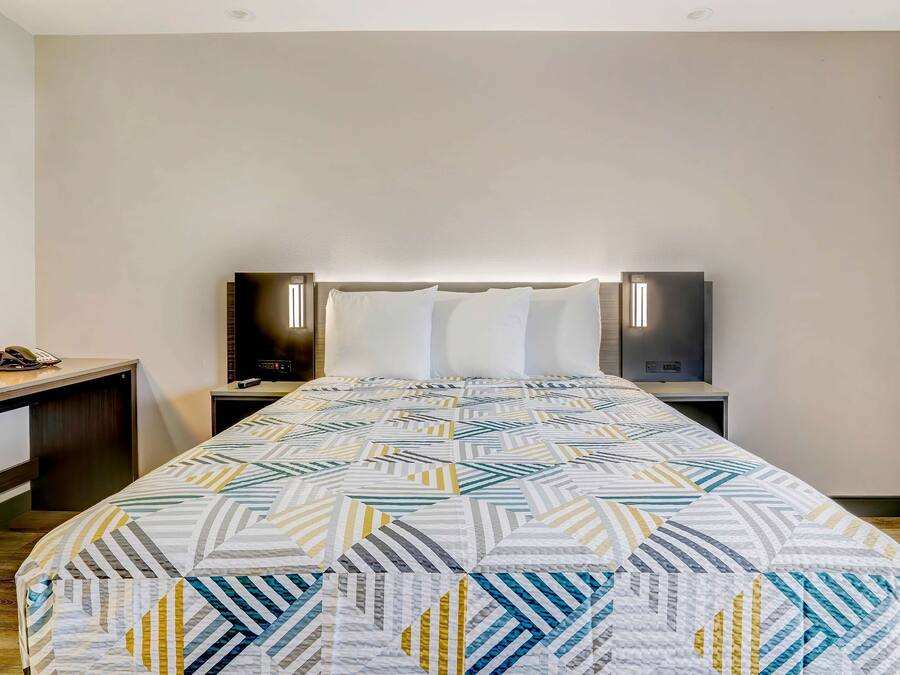 A hotel room with a bed, bedside tables, a desk, a lamp, and a phone.