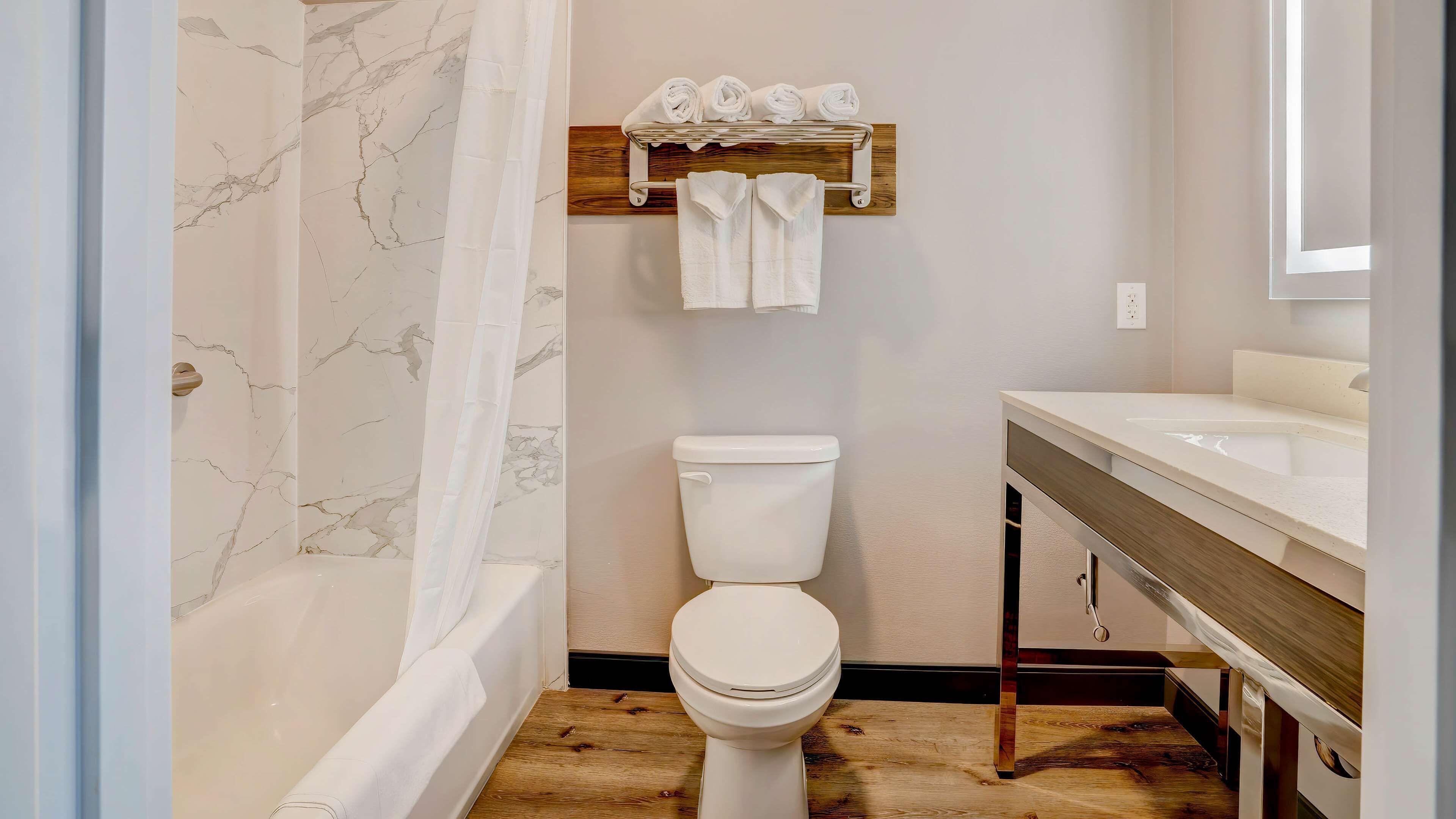 Un baño con pared de mármol, un inodoro, un estante de madera con toallas y suelo de madera.