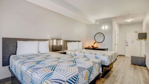Una camera d'hotel con due letti, una scrivania, una sedia, uno specchio e una televisione.