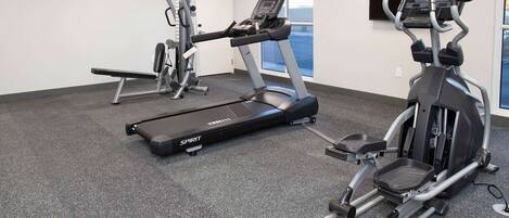 A gym with a treadmill, elliptical, and weight machines.