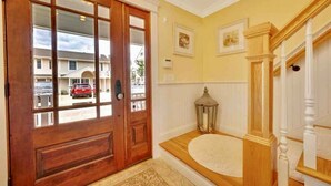 A wooden front door with glass panels, a white entryway with a rug, and a wooden staircase with white balusters. - Dream Beach House packed with Style, Comfort, and Convenience (Mantoloking)