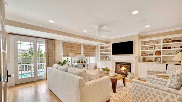 A spacious living room with a fireplace, a large TV mounted on the wall, and a balcony with glass doors. - Dream Beach House packed with Style, Comfort, and Convenience (Mantoloking)