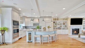 A spacious kitchen with white cabinetry, a central island with stools, and a fireplace. - Dream Beach House packed with Style, Comfort, and Convenience (Mantoloking)