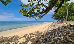 A beach with clear turquoise water, a sandy shore, and a stone wall.
