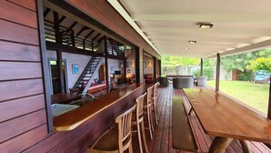 Un área de bar al aire libre con techo, bancos de madera y una escalera que sube a un nivel superior.