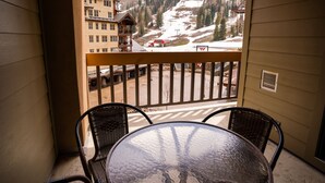 Een balkon met een tafel en stoelen, met uitzicht op een piste en gebouwen.