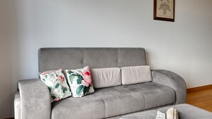 A grey sofa with floral cushions and a framed picture on the wall. - Tamariz Sea View, a Home in Madeira (Caniço)